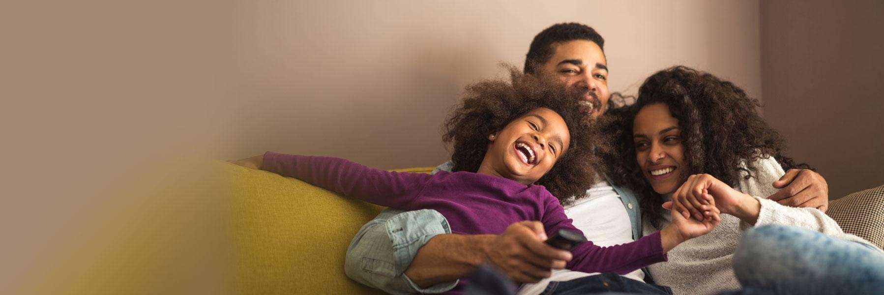 father, mother, and daughter laughing on the couch